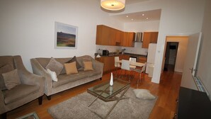 A modern living room with a glass coffee table, a sofa, and a dining area with chairs. - Belgravia Apartments - Gloucester Road (London)