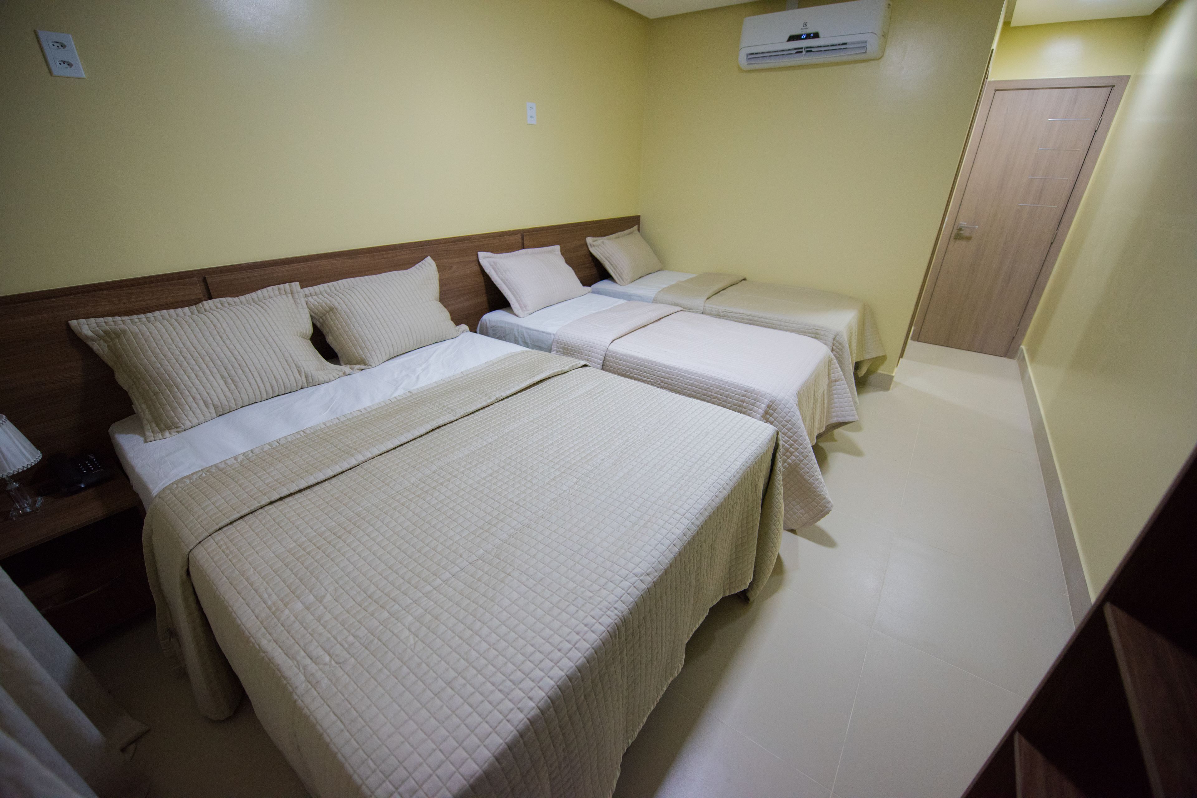 A hotel room with three beds, a wooden headboard, and a white tiled floor.