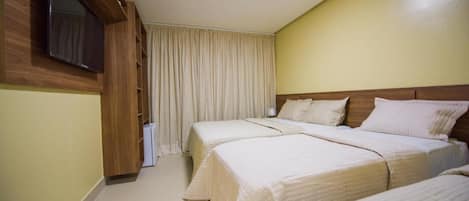 A hotel room with two beds, a TV mounted on a wooden panel, and a large window with curtains.