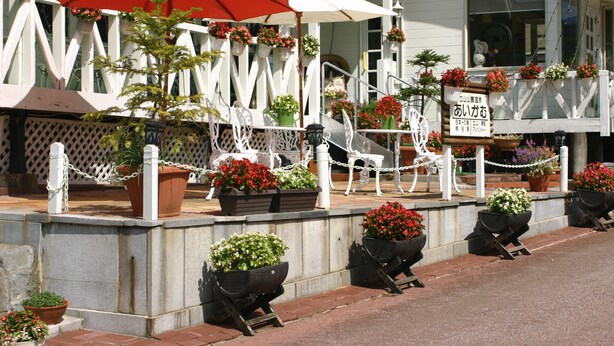 Un edificio de fachada blanca, con plantas en macetas y mobiliario exterior con sombrillas.