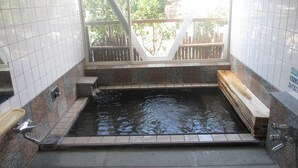 Zona de baño termal con paredes de azulejos, un banco de madera y vistas a la vegetación.