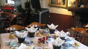 Un comedor con varias mesas dispuestas para una comida, sillas alrededor y una chimenea al fondo.