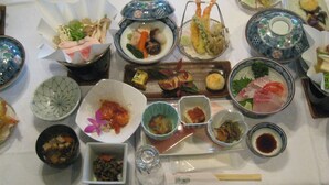 Una mesa con diversos platos, entre ellos sushi, sashimi y otras especialidades asiáticas, sobre un mantel blanco.
