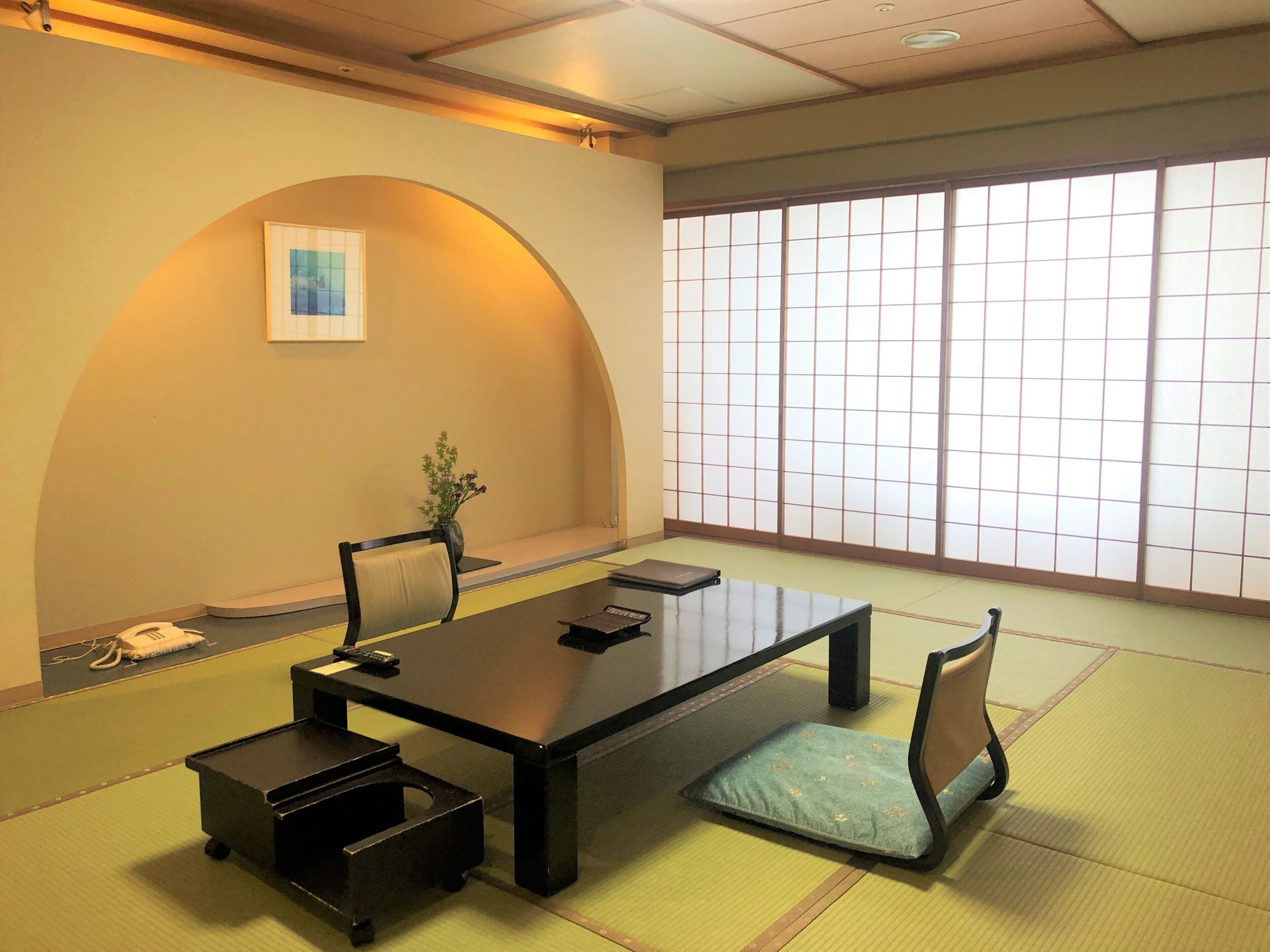 Une salle de réunion japonaise traditionnelle, avec un sol recouvert de tatamis, une table basse, des chaises, une petite plante et un paravent en papier de riz (shoji).