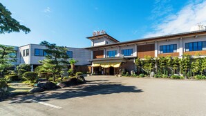 A traditional Japanese building with a large entrance, surrounded by greenery and a clear sky. - Yunomiko Onsen (Kamiichi)