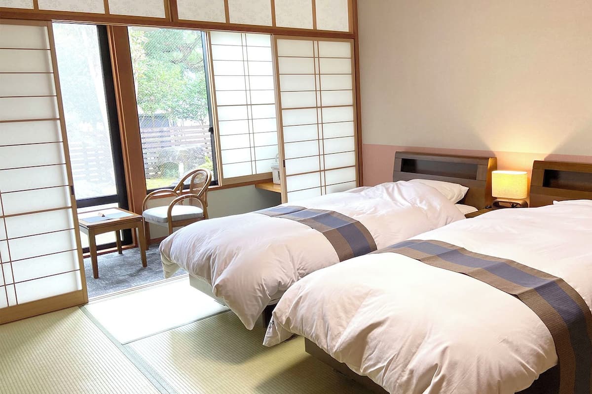 Ein Hotelzimmer mit zwei Betten, einem Sessel, einem Schreibtisch und einem verschiebbaren Shoji-Bildschirm.