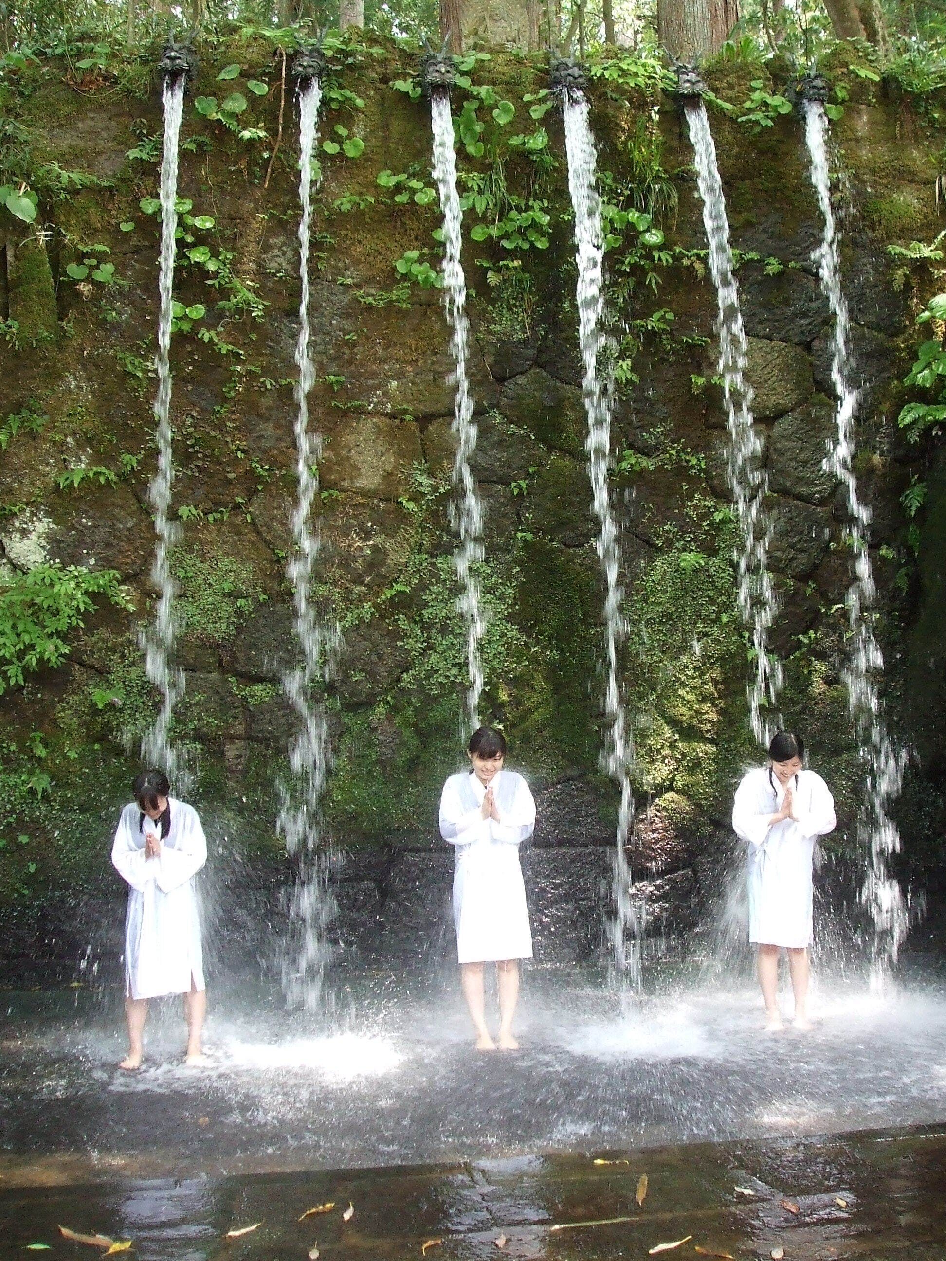 A waterfall with three individuals in white robes standing in front of it.