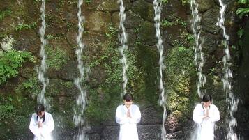 A waterfall with three individuals in white robes standing in front of it.