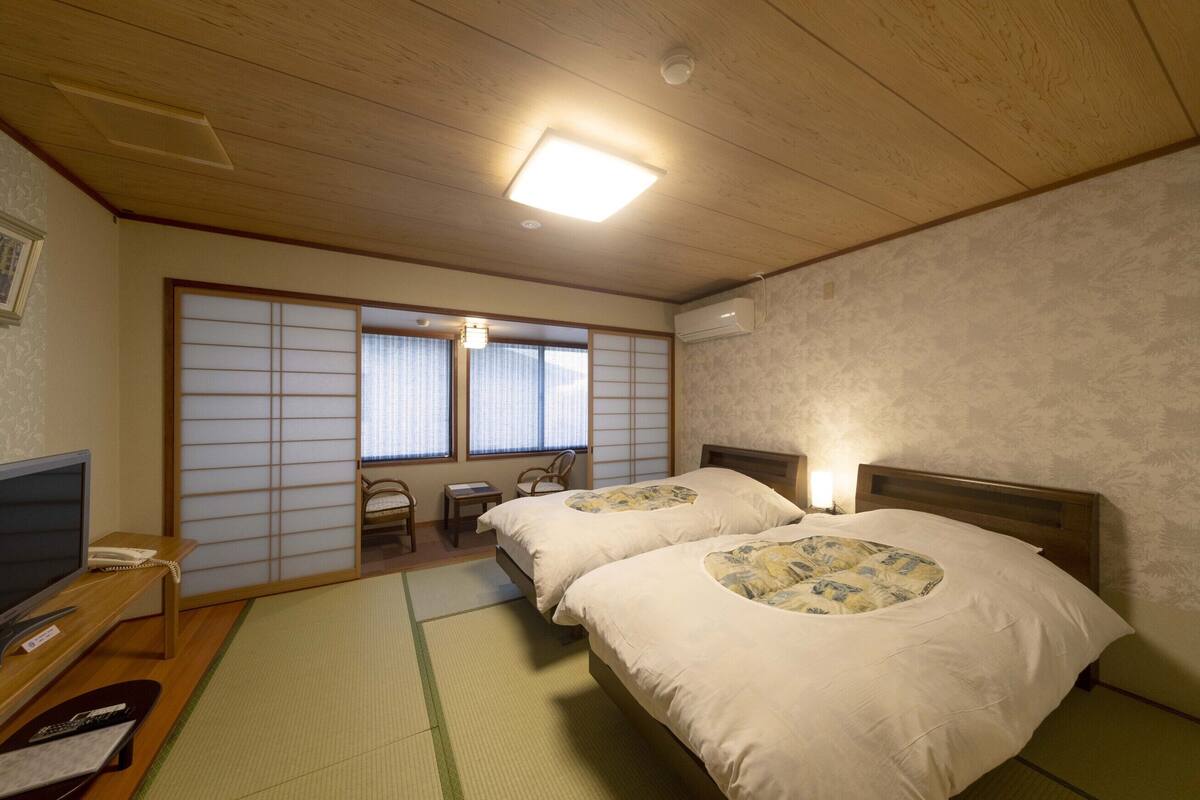 Ein traditioneller japanischer Raum mit Tatami-Boden, Futonbett, Fernseher und einer verschiebbaren Shoji-Schiebetür.