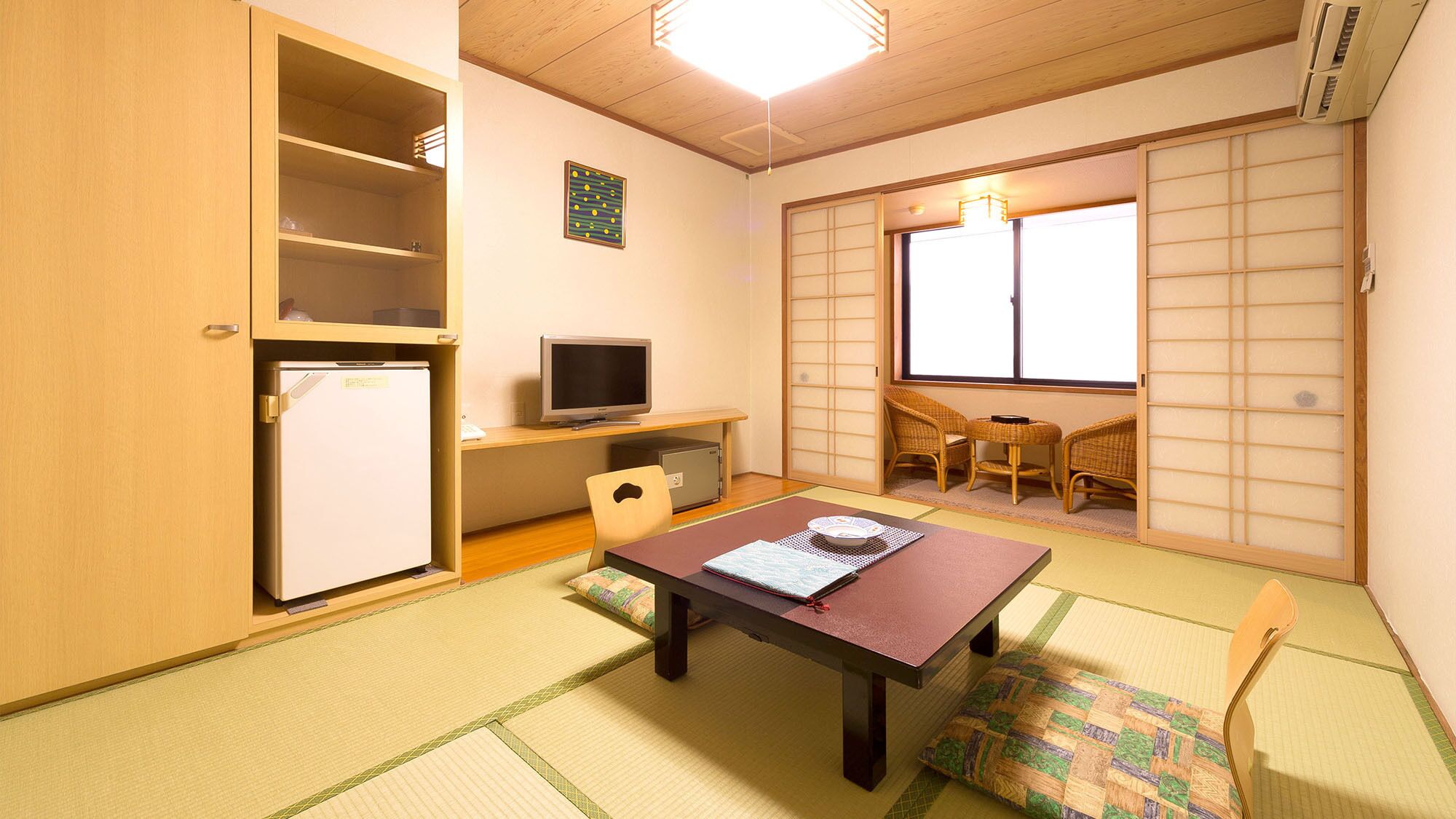 Habitació amb escriptori de fusta, televisió, nevera petita, sòl de tatami i porta corredissa amb panells shoji.