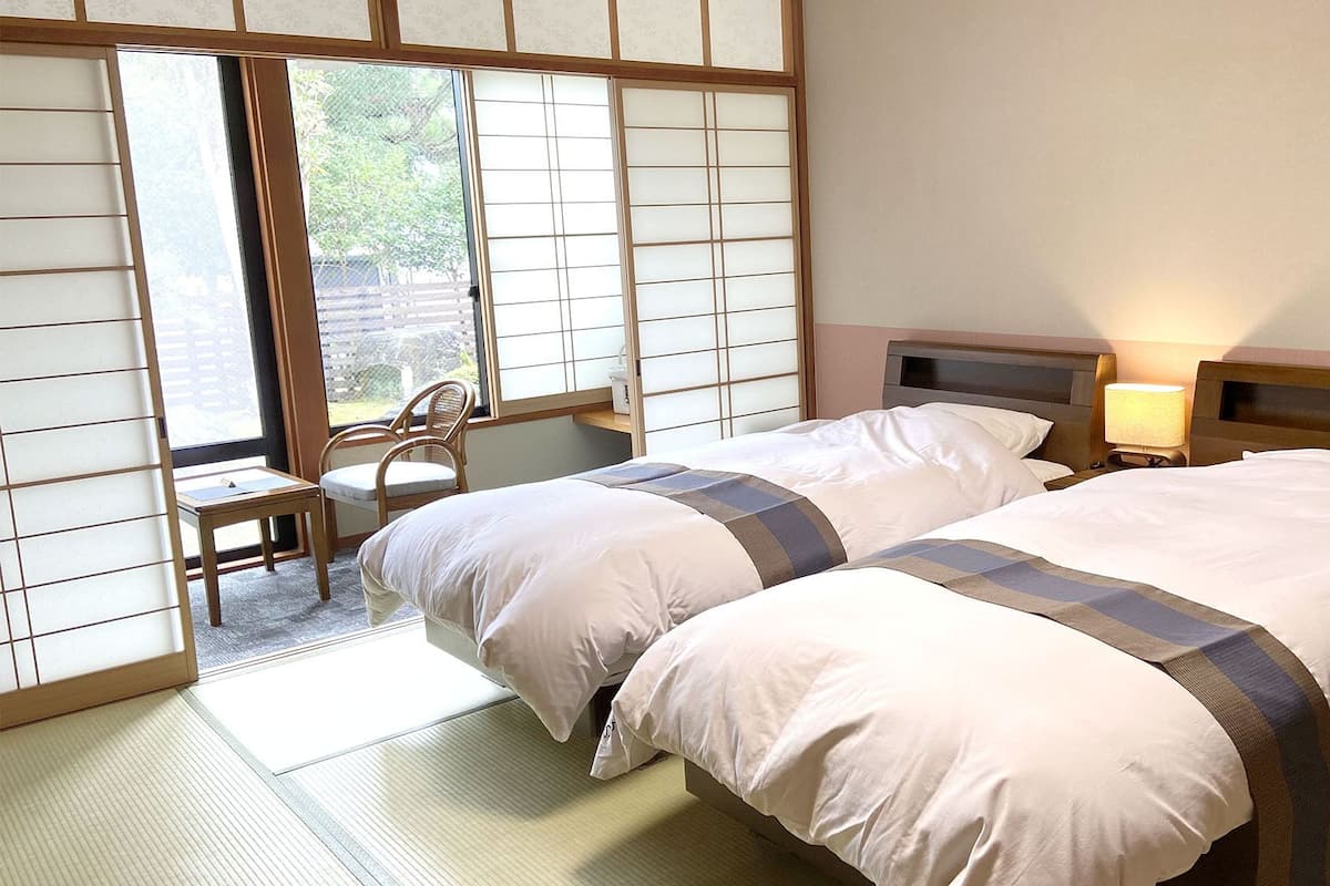 Ein Hotelzimmer mit zwei Betten, einem Sessel, einem Schreibtisch und einer Schiebetür mit Blick.