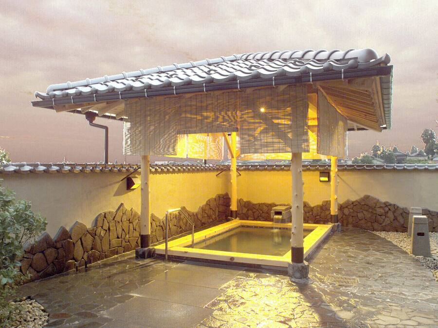 Un onsen japonès tradicional amb bany de pedra, teulada d'estuc i parets de fusta.