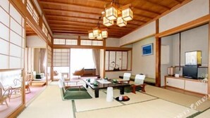 A traditional Japanese-style room with tatami flooring, a low table with cushions, a sofa, and a television on a cabinet. - Hotel Yoshihara (Toyama)