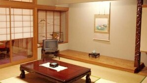 A traditional Japanese room with tatami flooring, a low wooden table, a television, and a small cabinet. - Hotel Yoshihara (Toyama)