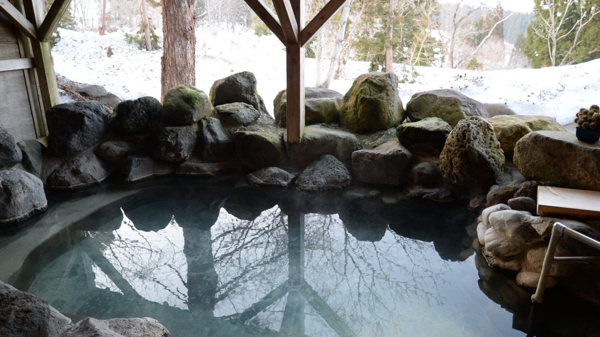 A hot spring area with a wooden structure, rocks, and a clear water pool.