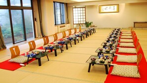 A long dining table with multiple chairs, arranged in a row, in a room with large windows and a framed artwork on the wall. - Kogakuro (Myoko)