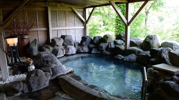 A hot spring area with a wooden structure, large rocks, and a small waterfall feature. - Kogakuro (Myoko)