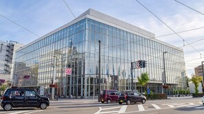 A modern glass building with a clear facade, located at a street intersection with cars passing by. - Hotel Shoen (Toyama)
