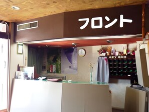 A reception desk with a 'KEY BOX' sign, a clock, and a window with a view of greenery. - Hotel Shoen (Toyama)