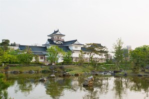 A traditional Japanese building with a prominent tower, surrounded by a pond with rocks and trees. - Hotel Shoen (Toyama)