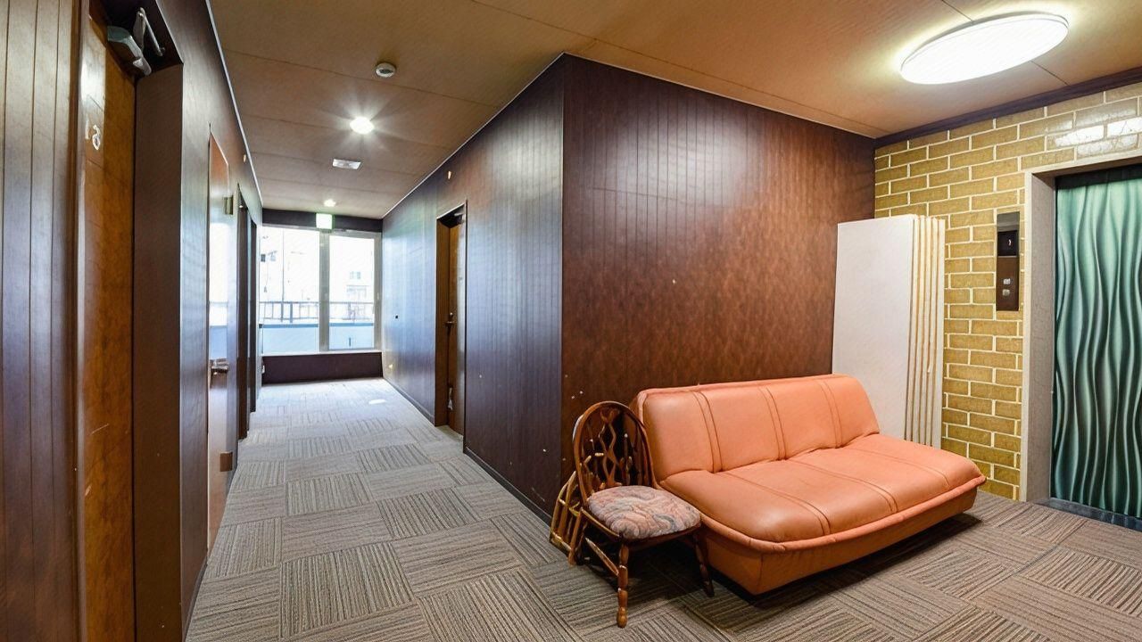 A hotel lobby with a long corridor, a wooden wall, a brick wall, a sofa, and a chair.