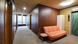 A hotel lobby with a long corridor, a wooden wall, a brick wall, a sofa, and a chair. - Hotel Shoen (Toyama)