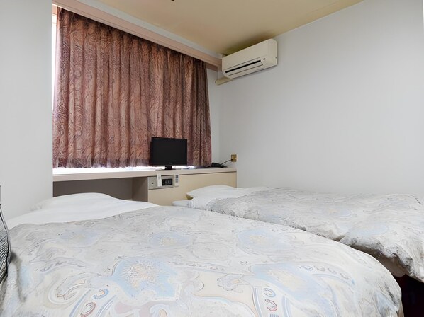 A hotel room with two beds, a desk with a computer, and an air conditioning unit. - Hotel Shoen (Toyama)