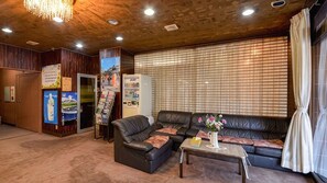 A room with a wooden ceiling, a black leather sofa, a small table with a vase, and a bulletin board with various notices. - Hotel Shoen (Toyama)