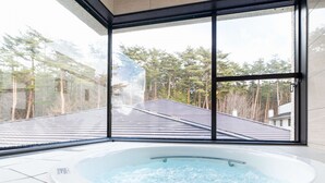 A hot tub with a clear view of a residential area through large windows. - Hotel Fuuka (Hokuto)