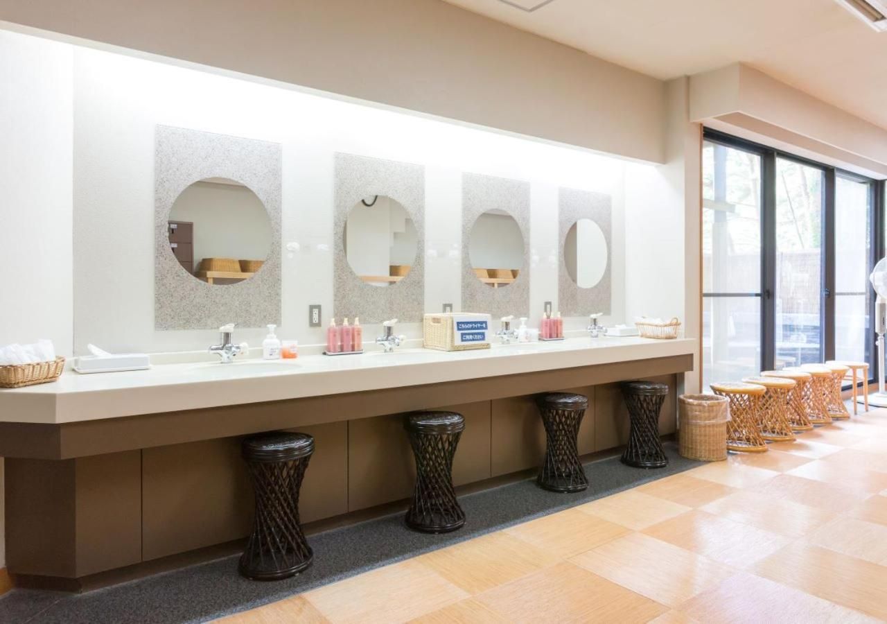 A hotel restroom with multiple sinks, each with a mirror, and a row of stools.