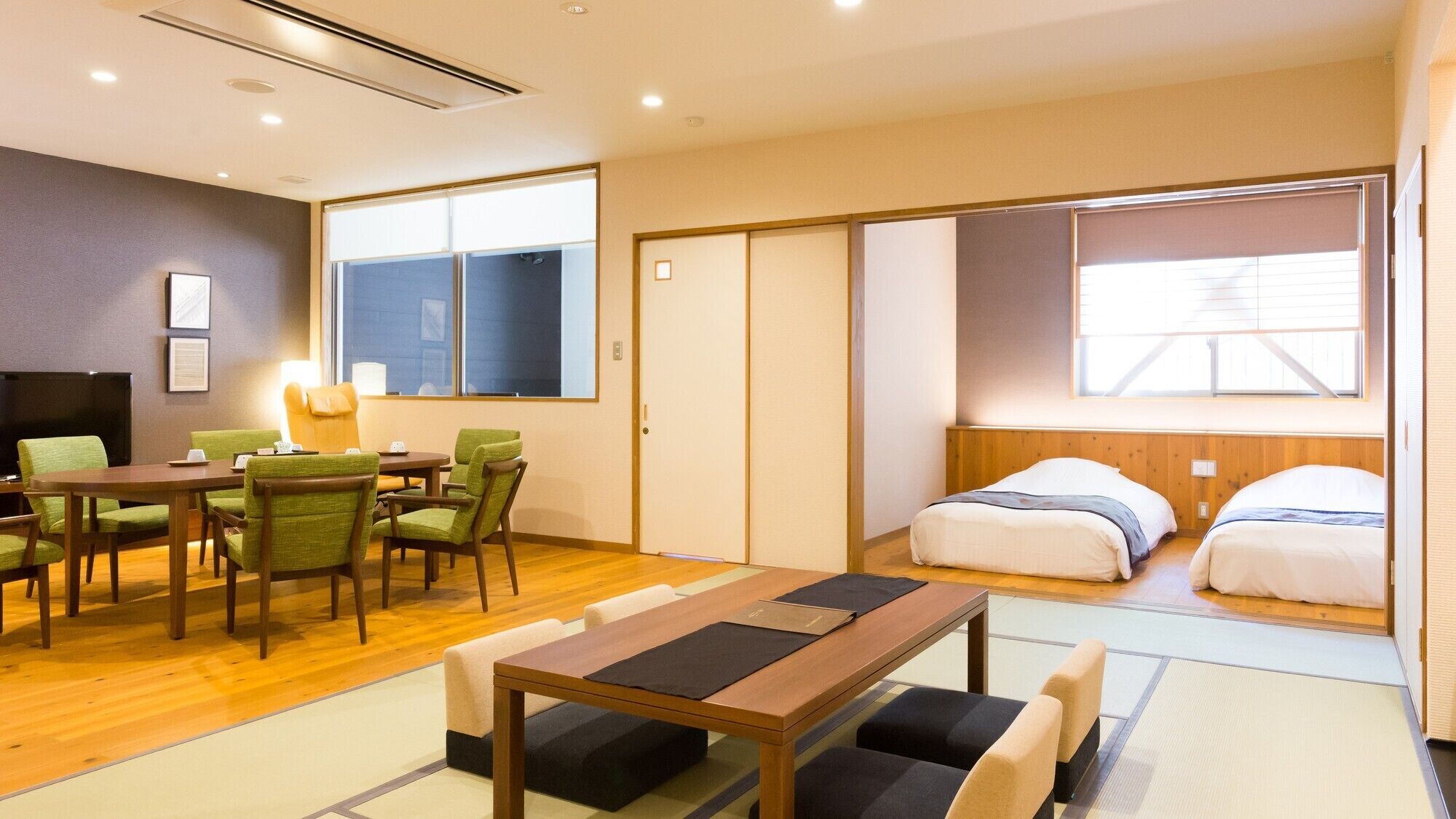Ein Hotelzimmer mit Holzboden, einem Bett mit weißer Bettwäsche, einem Schreibtisch mit Stühlen und einem Fernseher.