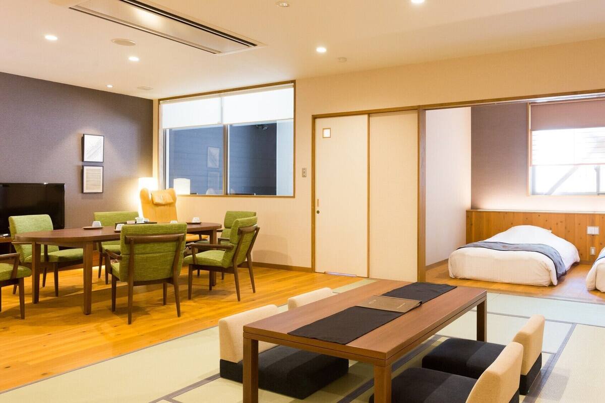 Ein Hotelzimmer mit Holzboden, einem Bett mit weißer Bettwäsche, einem Schreibtisch mit Stühlen und einem Fernseher.