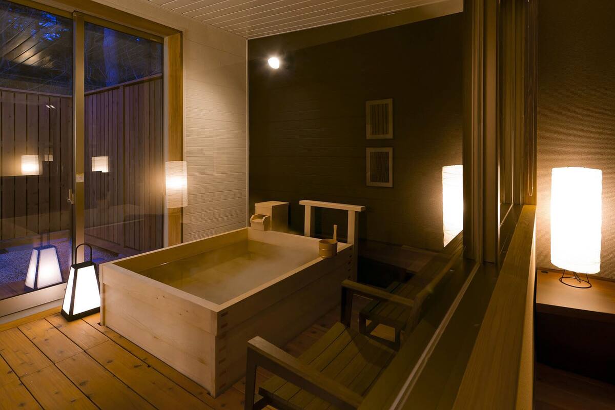 Ein Zimmer mit einer grossen Badewanne, Holzboden und Wandleuchten.
