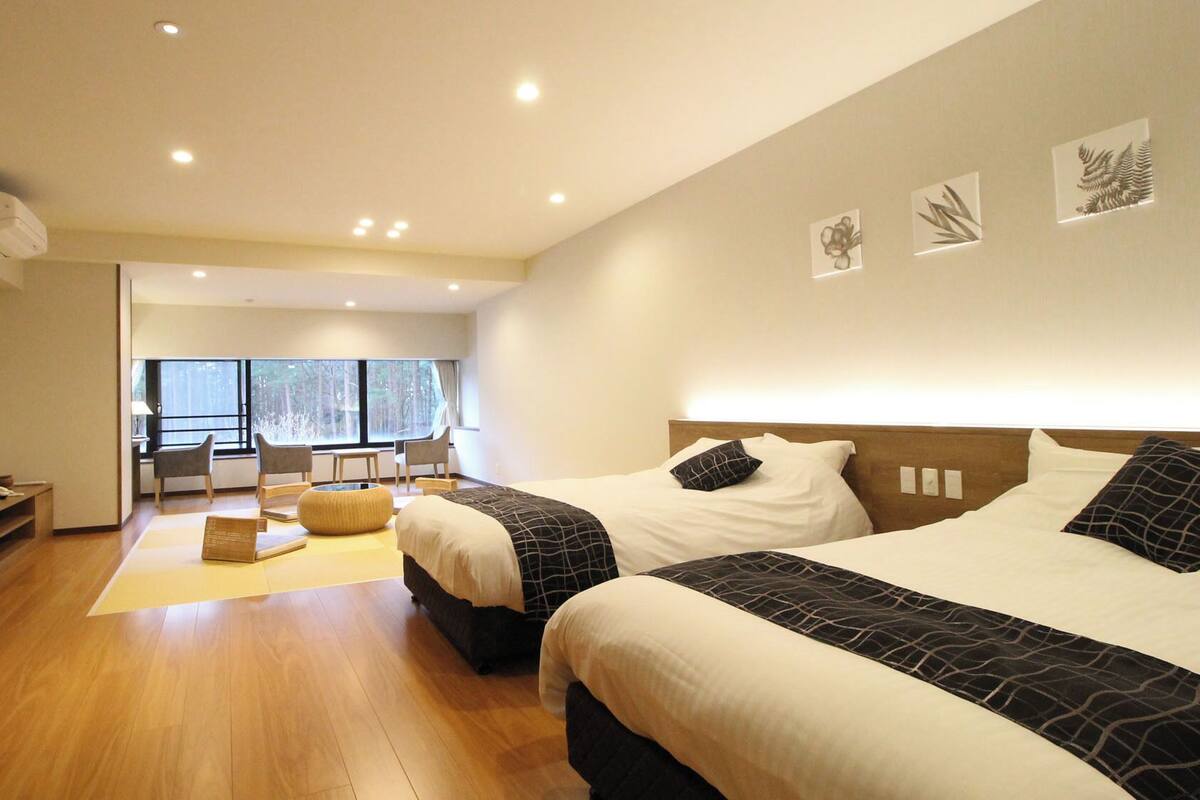 Ein modernes Hotelzimmer mit zwei Betten, einer Sitzecke und großen Fenstern.