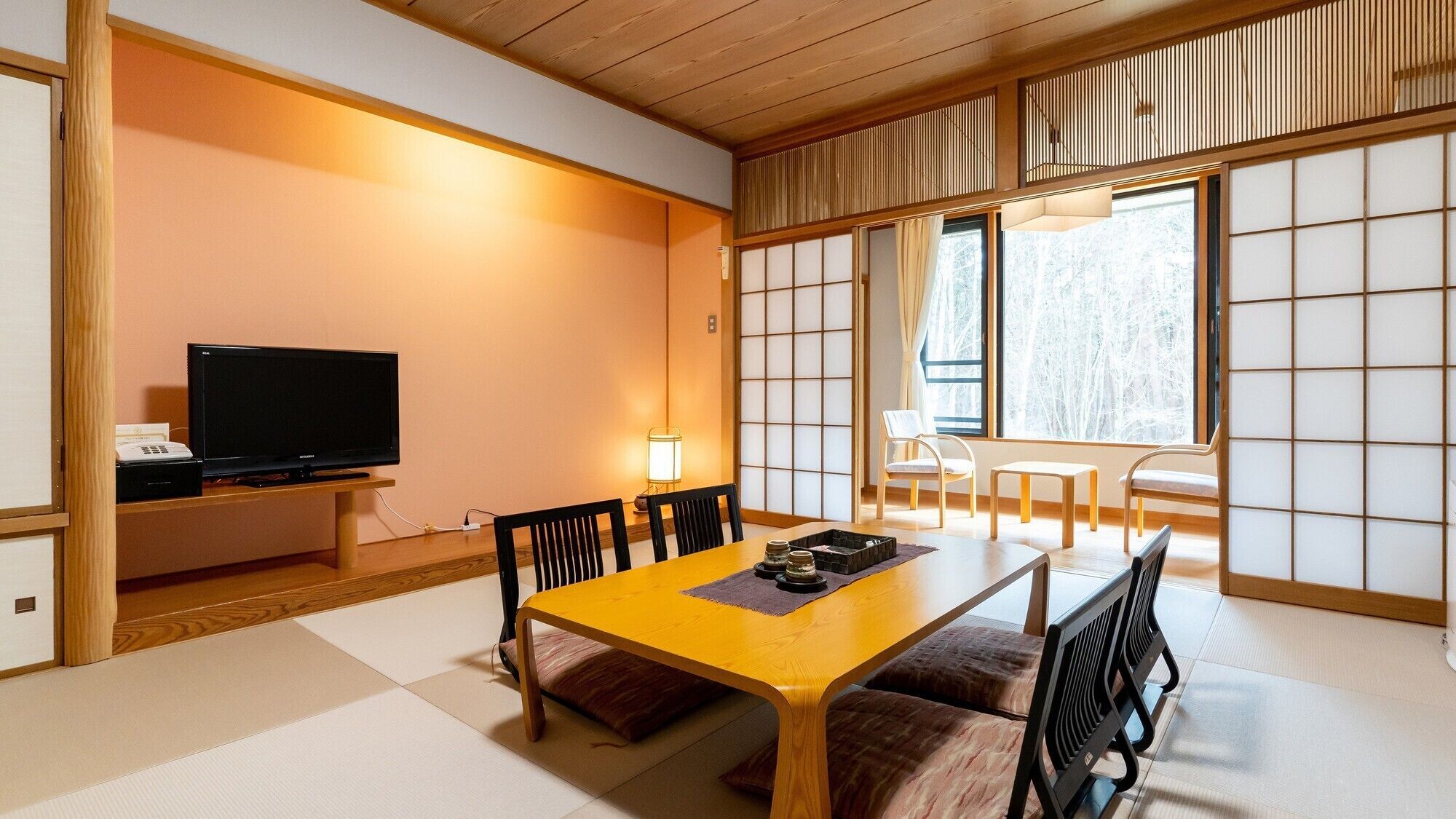 A traditional Japanese-style room with tatami flooring, a low table with cushions, a television, and sliding shoji doors.