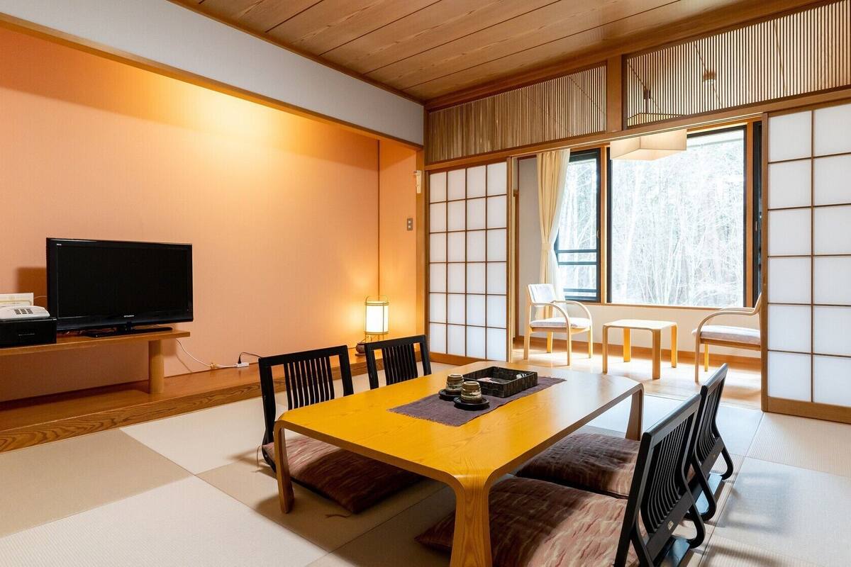 Ein traditioneller japanischer Raum mit Tatami-Bodenbelag, einem niedrigen Tisch mit Kissen, einem Fernseher und verschiebbaren Shoji-Türen.