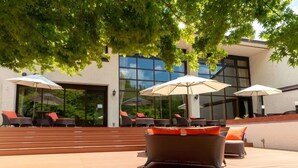 An outdoor seating area with wicker chairs and umbrellas, a staircase leading to a building with large windows. - Hotel Fuuka (Hokuto)