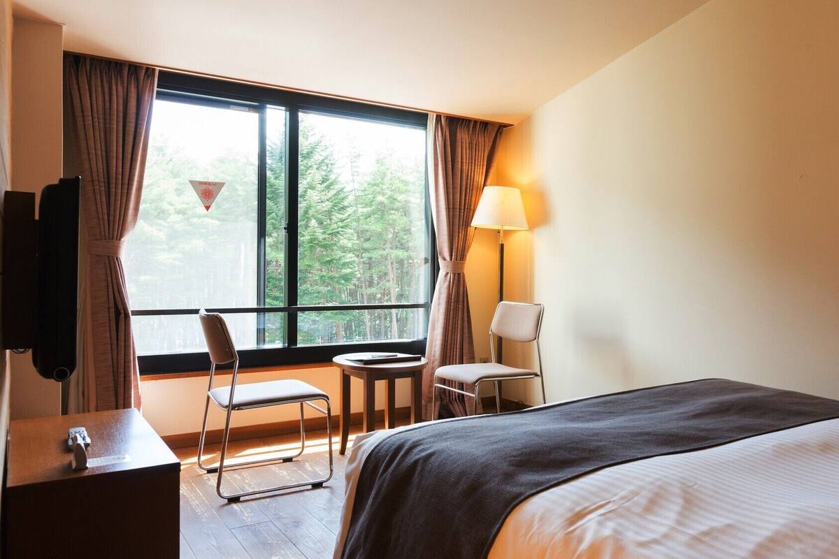 Ein Hotelzimmer mit Bett, Schreibtisch, Stuhl, Lampe und einem Fenster mit Vorhängen.