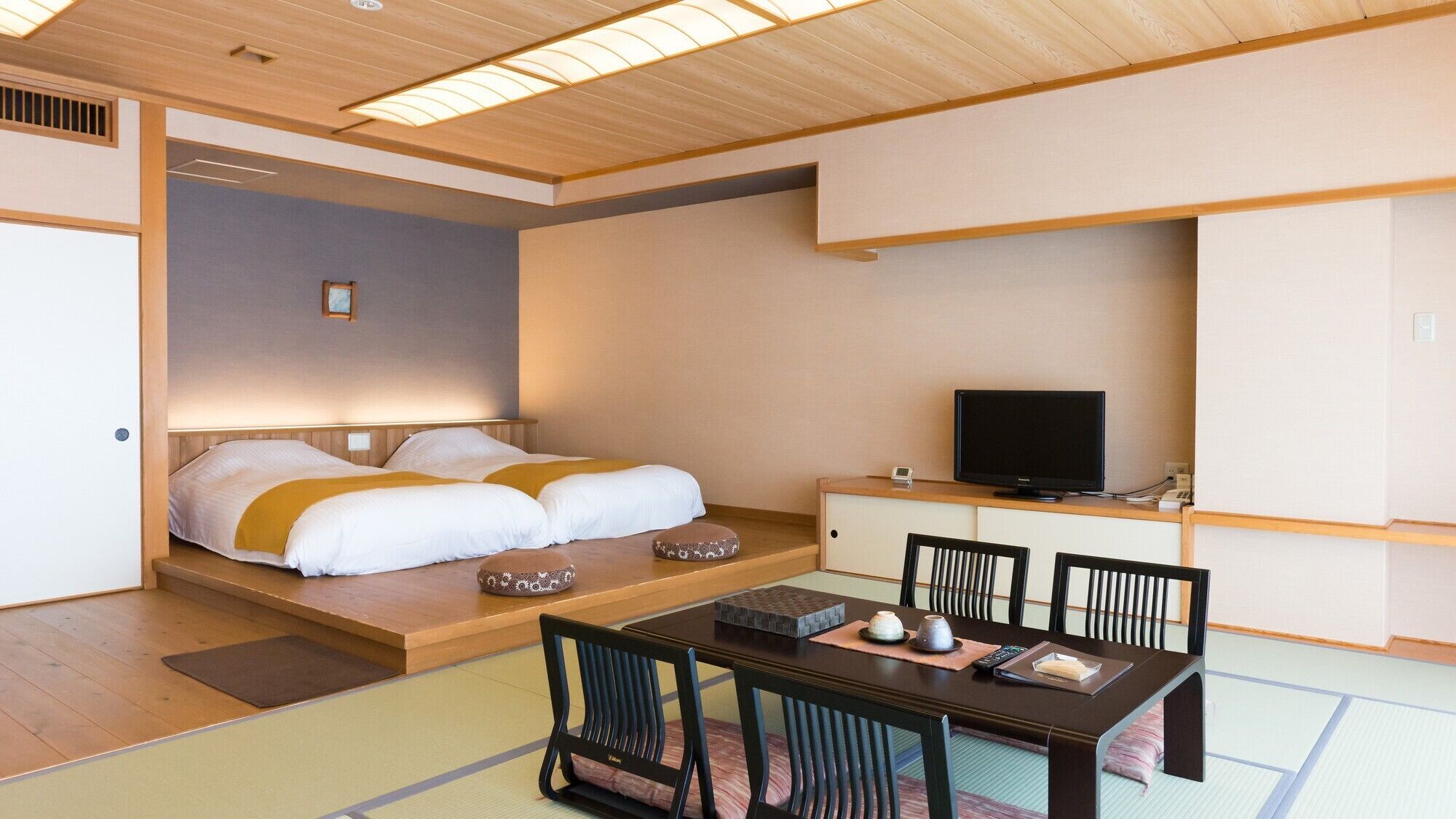 Ein Hotelzimmer mit einem Bett, einem Fernseher, einem Esstisch mit Stühlen und einer kleinen Kommode.