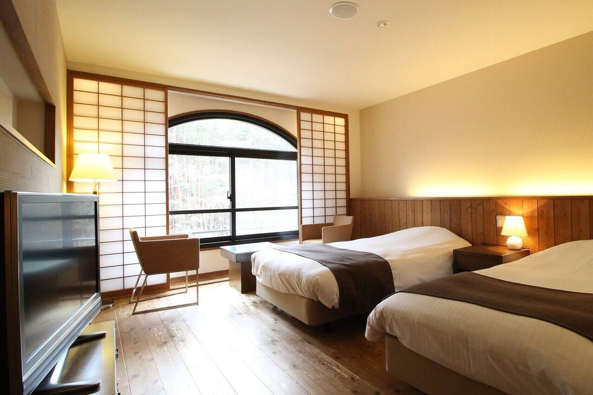 Ein Hotelzimmer mit zwei Betten, einem Schreibtisch, einem Fernseher und einem großen Fenster mit Blick.