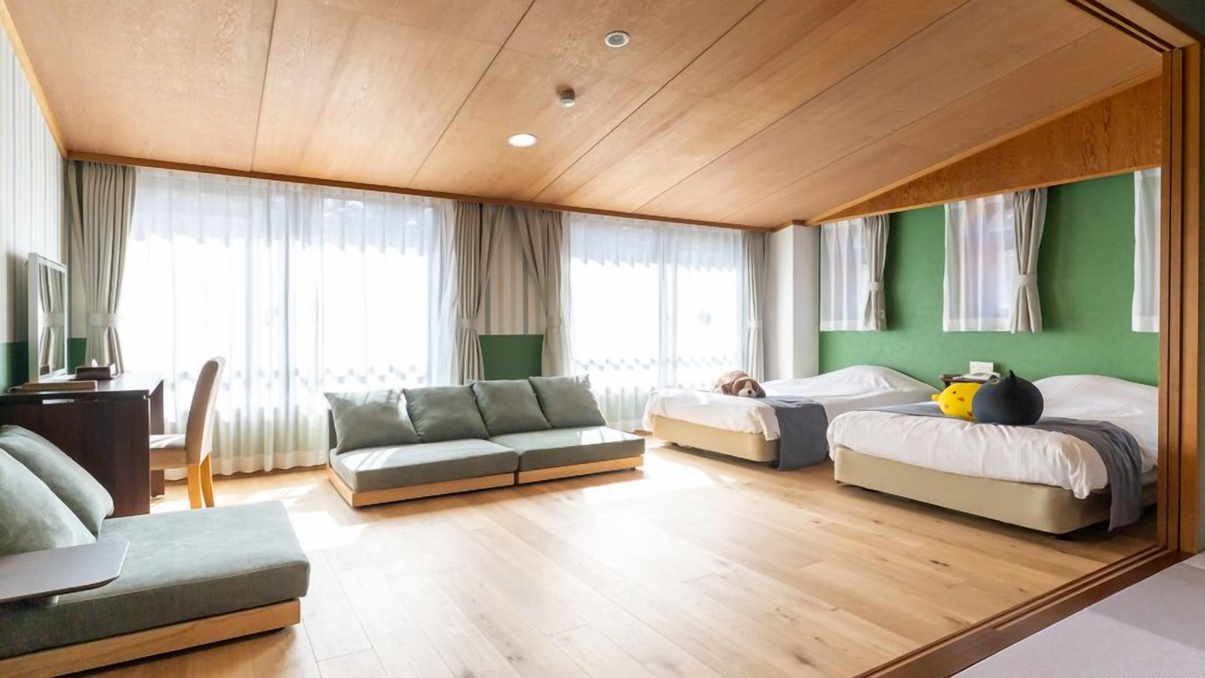 Ein modernes Hotelzimmer mit Holzbalkendecke, zwei Betten, einer Sitzecke und einem Schreibtisch.