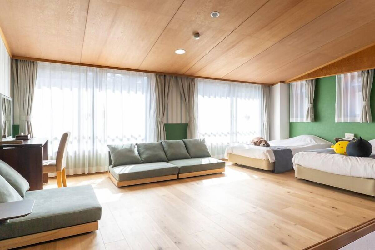 Ein modernes Hotelzimmer mit Holzbalkendecke, zwei Betten, einer Sitzecke und einem Schreibtisch.