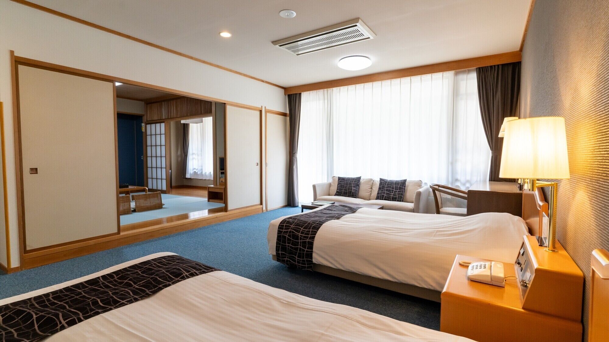 Ein Hotelzimmer mit zwei Betten, einem Schreibtisch, einer Lampe, einem Telefon und einem großen Spiegel.