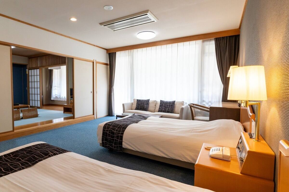 Ein Hotelzimmer mit zwei Betten, einem Schreibtisch, einer Lampe, einem Telefon und einem großen Spiegel.