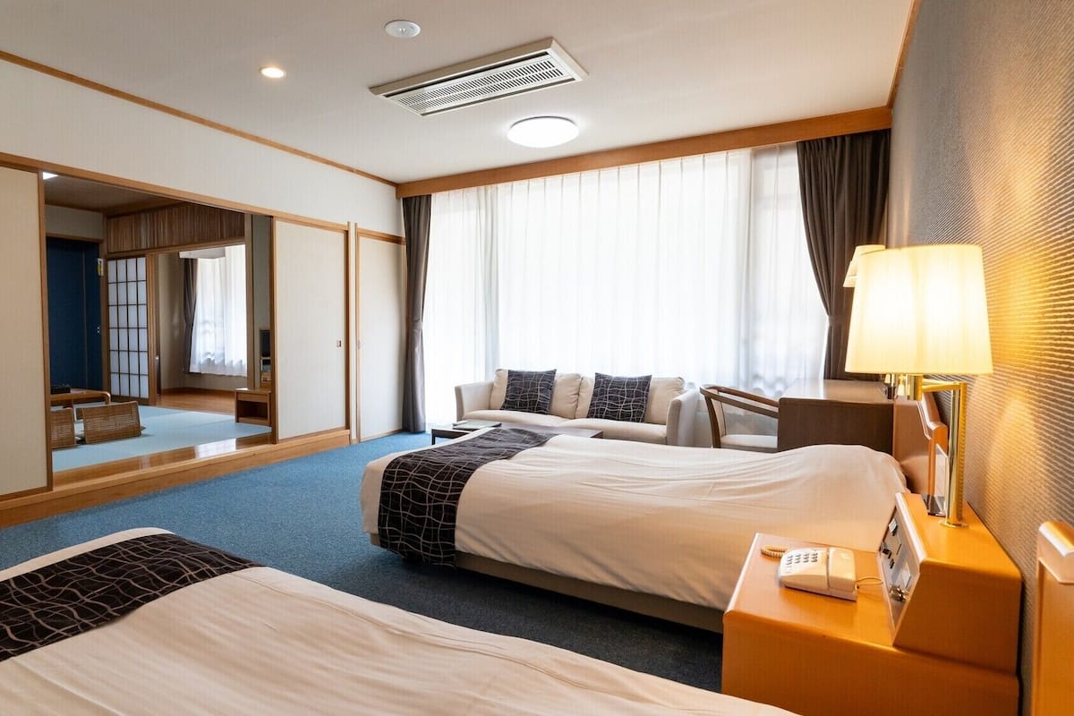 A hotel room with two beds, a desk, a lamp, a phone, and a large mirror.
