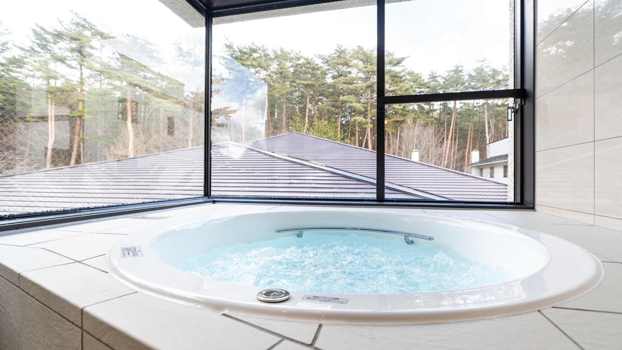 Ein Whirlpool mit freiem Blick auf einen Wald durch große Fenster.