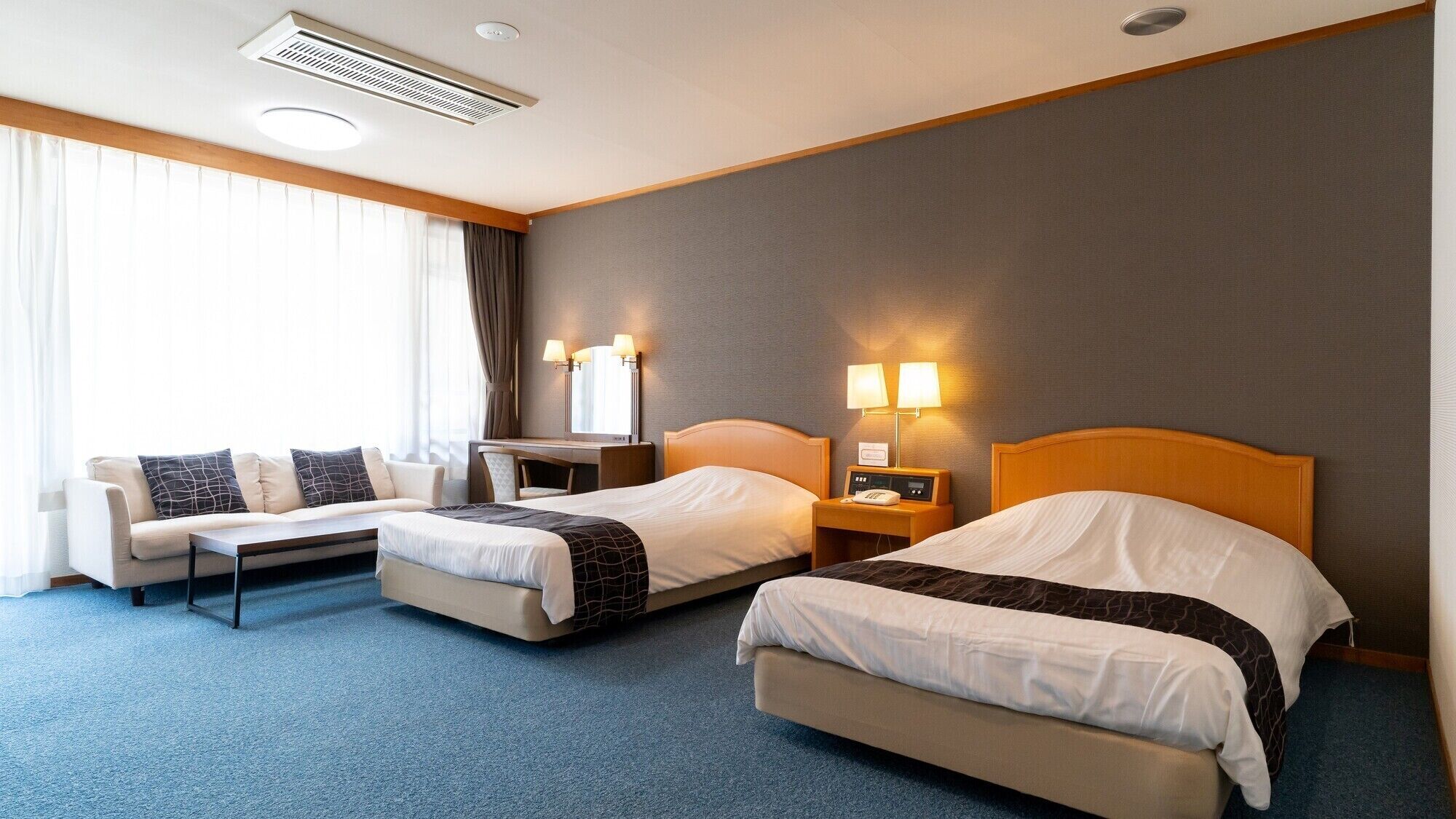Ein Hotelzimmer mit zwei Betten, einem Sofa, einem Schreibtisch und einer Lampe.
