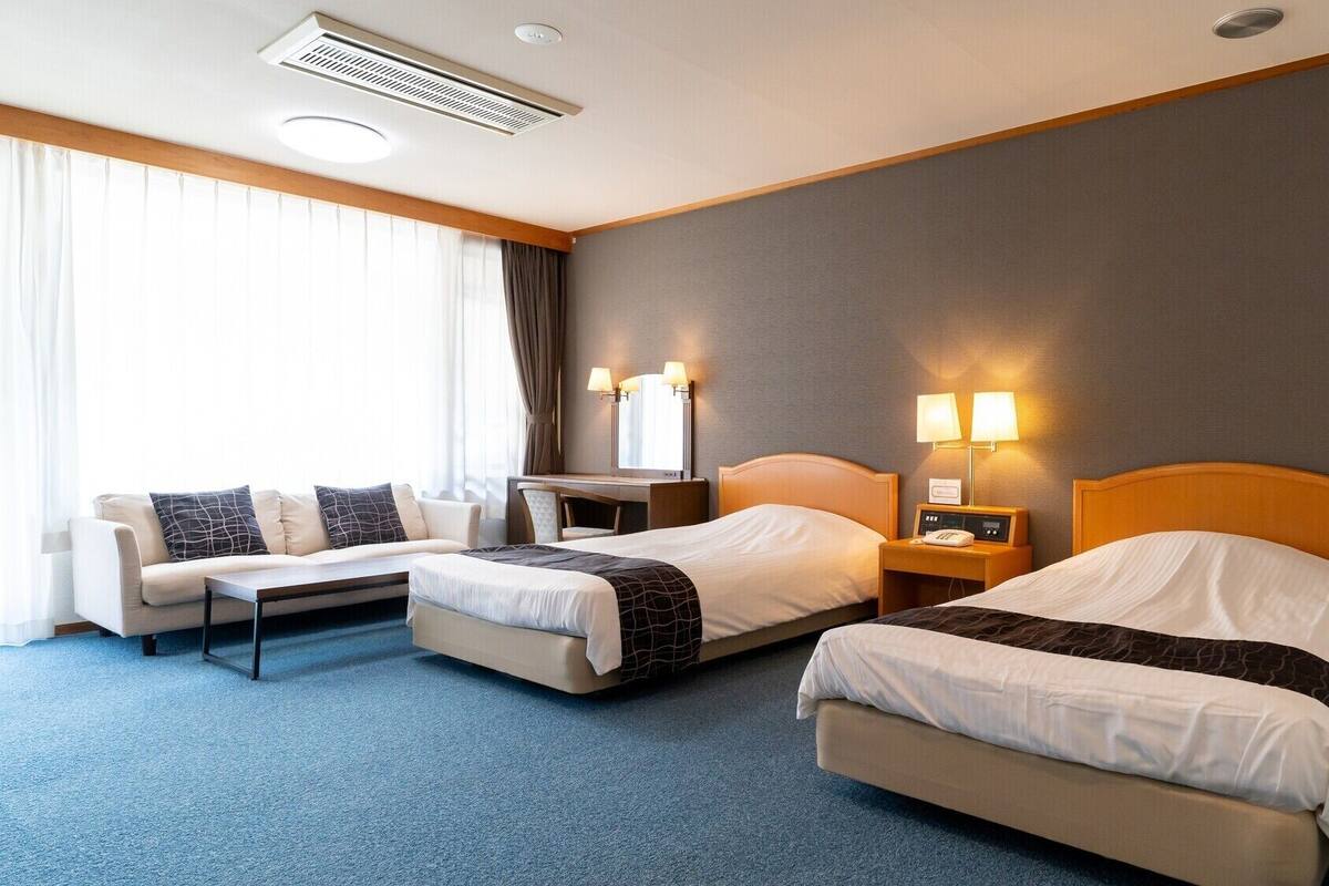 Ein Hotelzimmer mit zwei Betten, einem Sofa, einem Schreibtisch und einer Lampe.