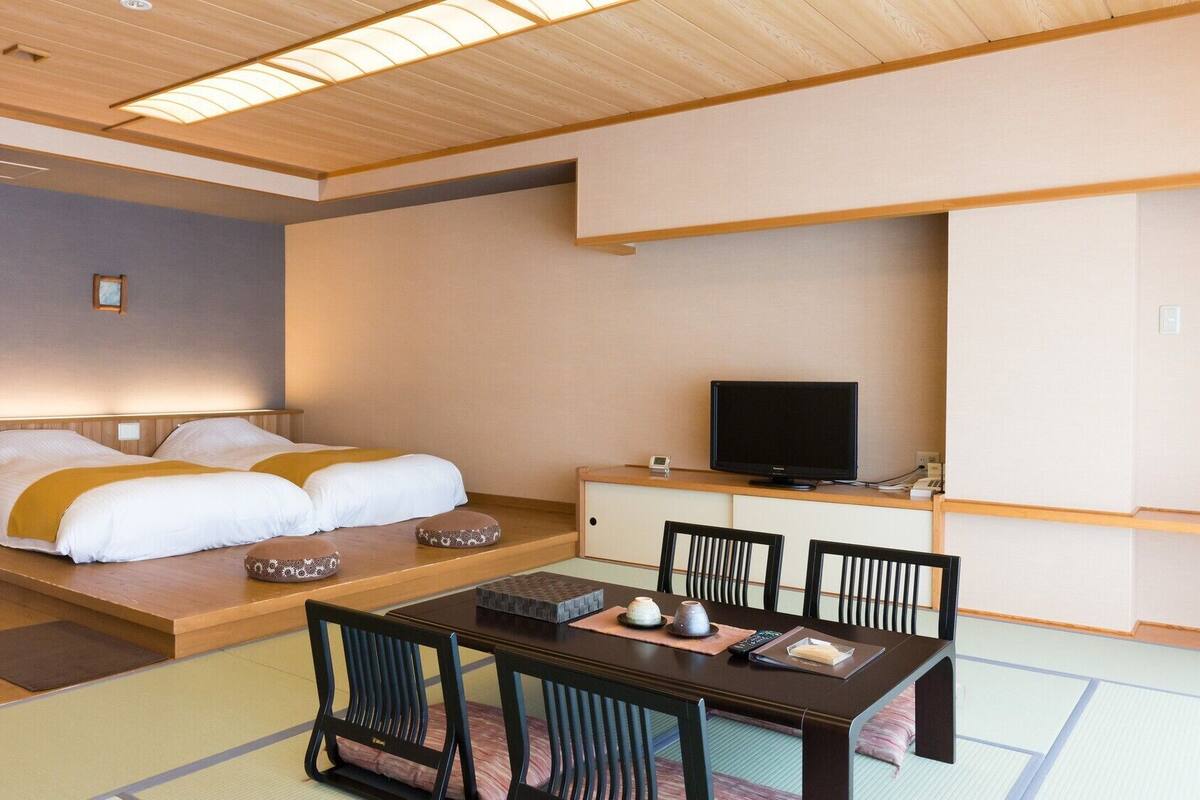 Ein Hotelzimmer mit einem Bett, einem Fernseher, einem Esstisch mit Stühlen und einer kleinen Kommode.