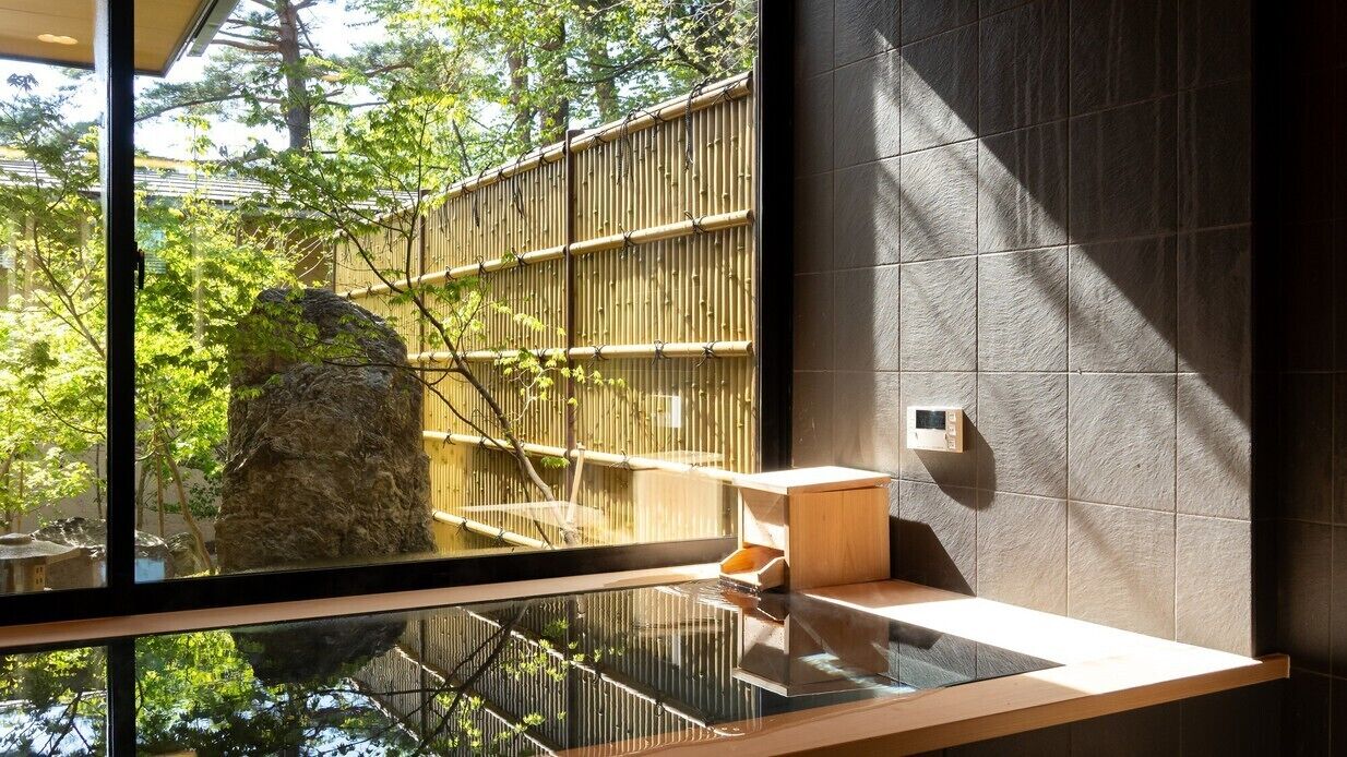 Ein modernes Badezimmer mit großem Fenster, einer Holzbank und einem Steinornament.